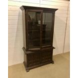 A dark oak display unit with cupboards under and above with glazed doors and internal shelves by