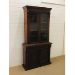 A tall oak bookcase with upper glazed doors and carved detailing, with a drawer and cupboard under