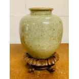 An oriental pot with green glaze and wooden stand