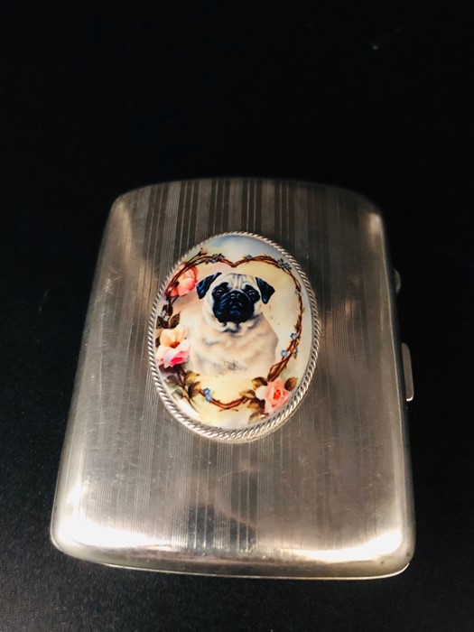 A silver cigarette case with enamel image to the front in the form of a dog.