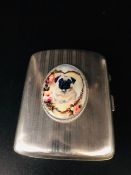 A silver cigarette case with enamel image to the front in the form of a dog.