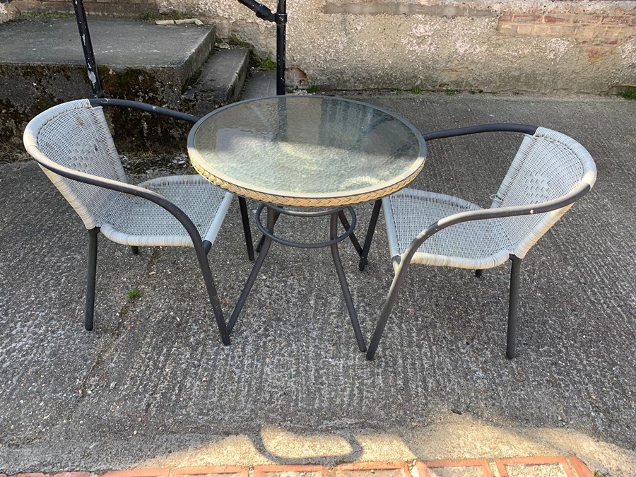 A rattan style bistro set with glass top and two chairs