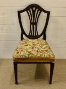 An oak hall chair with shield shaped back and inwardly curved splats with a needlework upholstered