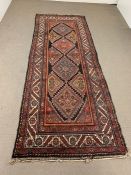 A red, orange and blue coloured runner with a diamond pattern to center (296cm x 110cm)