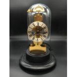 A Kieninger Skeleton Bell Chime Clock under a glass dome.