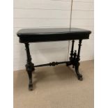 An ebonized library/tea table with twin end supports, jointed by a turned pole stretcher (H72cm