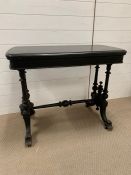 An ebonized library/tea table with twin end supports, jointed by a turned pole stretcher (H72cm