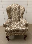 An upholstered wing back chair with mahogany feet