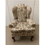 An upholstered wing back chair with mahogany feet