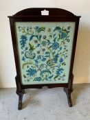 A mahogany fire screen with floral needlework under glass