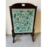 A mahogany fire screen with floral needlework under glass