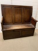 An 18th Century Oak settle, three panelled back above a hinged seat H 120cm x W 126 cm x D 47cm