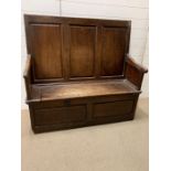 An 18th Century Oak settle, three panelled back above a hinged seat H 120cm x W 126 cm x D 47cm