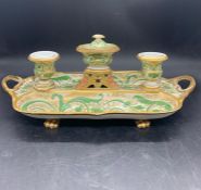 A porcelain desk stand with lidded inkwell to the center and two candlesticks with pen trays on both