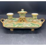 A porcelain desk stand with lidded inkwell to the center and two candlesticks with pen trays on both