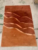 A hand knotted and made in Nepal red and orange rug with wave design through centre (178cm x 120cm)