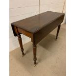 A mahogany hall table with drop sides and turned legs terminating with brass castors
