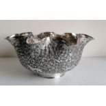 An Indian white metal circular bowl with wavy rim, elaborately embossed with elephants, tigers,