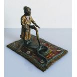 An early 20th Century cold painted bronze depicting a snake charmer and snake on a polychrome carpet