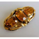 A Victorian three-stone citrine brooch on an elliptical gold frame with etched foliate decoration,