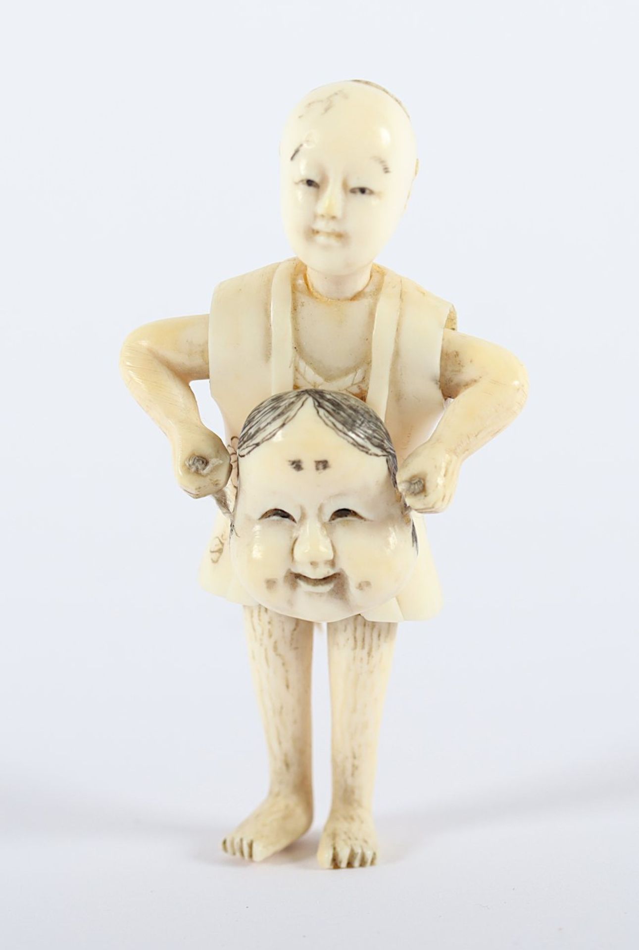 OKIMONO KIND MIT MASKE, Elfenbein, mehrteilig, ein Knabe hält mit beiden Händen eine Okame-Maske,