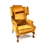 An 18th century style walnut wing-back armchair upholstered in studded gold velour and on carved