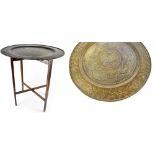 A Benares-style brass circular table top on hardwood folding support, diameter 66cm.
