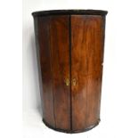 An 18th century walnut bow front corner cupboard with twin doors enclosing shell canopy and three