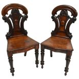 A pair of Victorian mahogany hall chairs with carved backs and shaped seats on turned and tapered