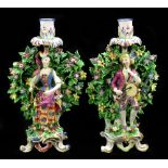 DERBY; a pair of 18th century figural candlesticks with large sections of bocage and raised on