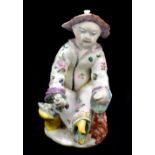 CHELSEA; a mid 18th century figure of a seated Chinese gentleman with two fish upon a pot by his