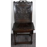 A late 17th century oak back stool with carved panel, plank seat and turned front legs united by