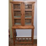 A pine side cabinet, the upper section with twin glazed doors above a base raised on square