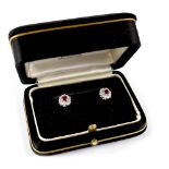 A pair of white metal floral ear studs set with central ruby-coloured stone and white stones.