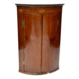 A George III mahogany bow-front wall-hanging corner cupboard, inlaid with shell motifs,