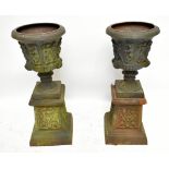 A pair of reproduction cast iron urns modelled with figural friezes in relief on socle bases,