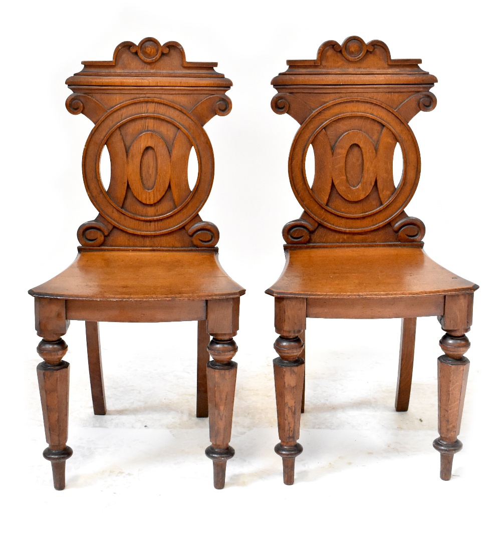 A pair of 19th century oak hall chairs, the backs with carved circular motifs,