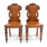 A pair of 19th century oak hall chairs, the backs with carved circular motifs,