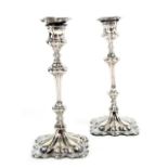 A pair of white metal candlesticks, slender column supports to floral stepped bases,