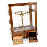 A cased set of Oertling brass apothecary scales within a glazed oak case, height 56cm, width 43cm,