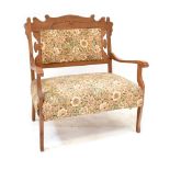An Edwardian oak-framed settee of small proportions with carved back rest and upholstered in a