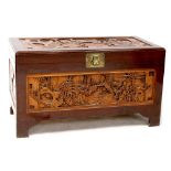 A Chinese camphor wood blanket box with carved panels depicting figures within landscapes,