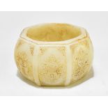 A pale green jade octagonal bowl, the body divided into panels with each featuring an auspicious