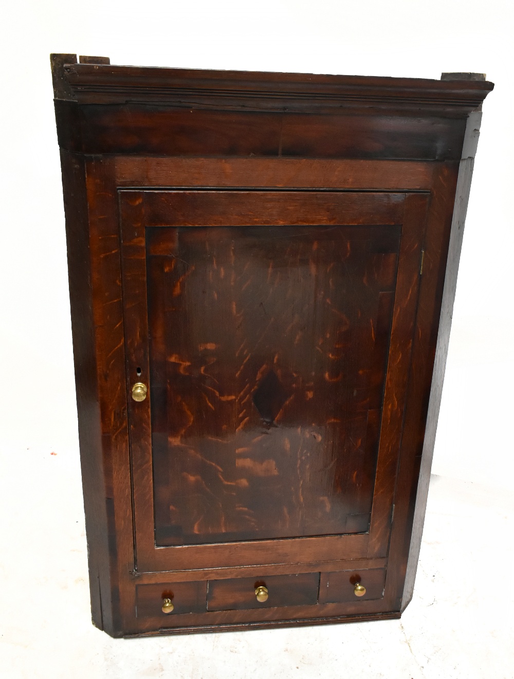 An 18th century oak flat fronted hanging corner cupboard, the single panelled door above three