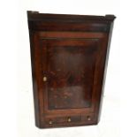 An 18th century oak flat fronted hanging corner cupboard, the single panelled door above three