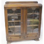 A 1930s oak glazed bookcase with a pair of panelled doors with carved motifs above two short