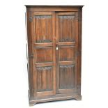 An early 20th century oak wardrobe, the pair of linen fold carved doors enclosing rail, raised on