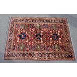 A Caucasian hand knotted wool rug decorated with geometric motifs against a red ground, 180 x 129cm.