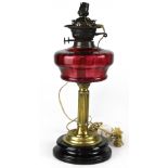 An Edwardian cranberry glass oil lamp on a reeded brass column and turned wooden base,