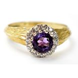 A vintage 18ct gold ring with central claw set amethyst stone in a halo of small white stones,